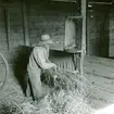 Nilsson repar takhalm på halmrepan i logen. Ovanför halmrepan hänger en ljuskista för kådljus, som stacks in i ett hål i botten. Ljuset sattes i underifrån.