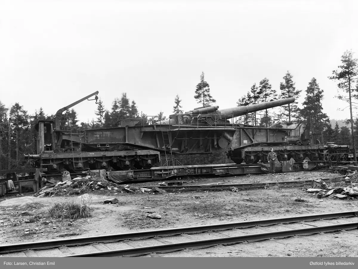 Kanon på jernbanevogn, batteriet på Knatterud, Varteig ved Sarpsborg 1945. De to jernbanekanonene ble forsøkt plassert på to fundamenter på Strand gård i daværende Onsøy kommune fra høsten 1942, for å beskytte Fredrikstad havn. Det ene fundamentet ble for dårlig pga kvikkleire, og høsten 1943 ble kanonene flyttet til Knatterød.
Soldat, ukjent.
Deutsche Reichsbahn, Berlin.

Dette er en "28 cm kanon Schwere Bruno" Den hadde en totallengde på 22.8 meter og en vekt på 118 tonn. Lengden på kanonrøret 11.93 meter. 
Utgangshastighet på granaten var 860 m/sek. Maks skuddvidde 37.8 km. Skuddhastighet ca 10 skudd i timen.  Kilde: Østfold Historielags tidsskrift WIWAR nr1 2002.