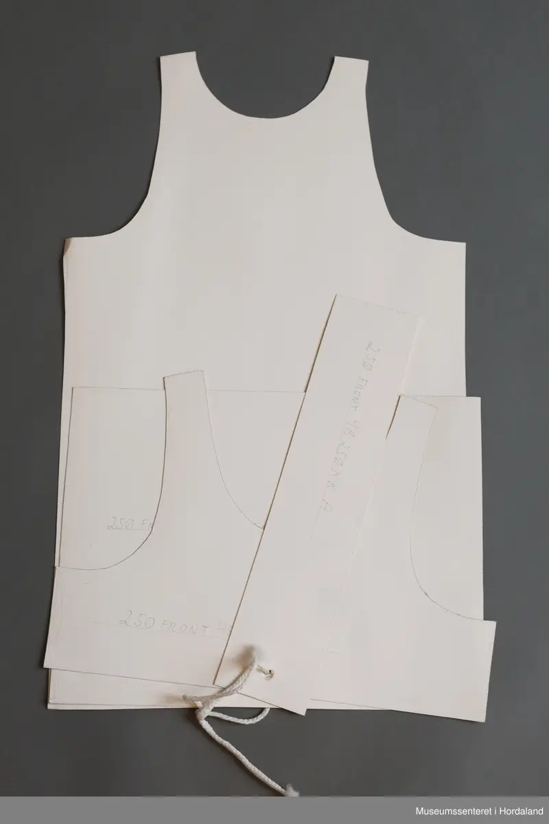 Mønsterskantar i papp, brukt til å skjere ut ulike delar av plagg i klesproduksjon. Desse er til ein singlet.