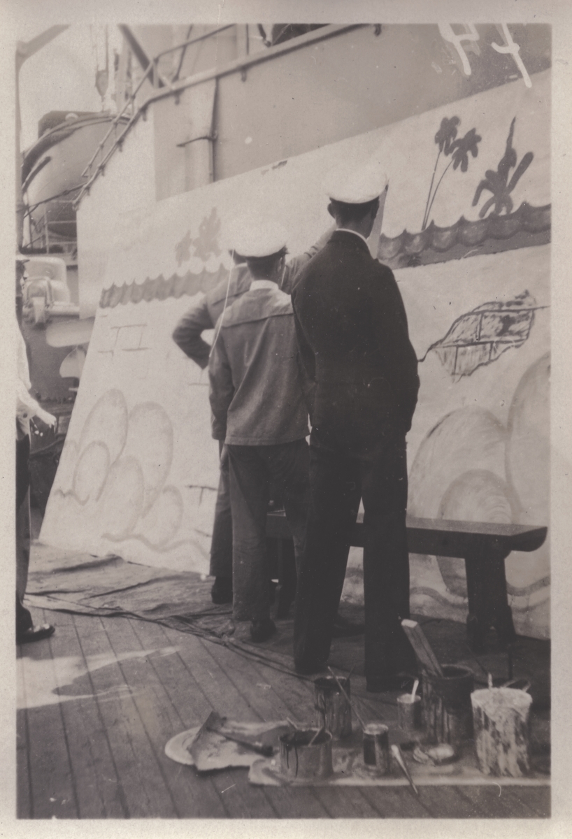 Tre officerare (?) ombord på fartygsdäck betraktar stor målning (teaterdekor?). Tid, plats och sammanhang okända.