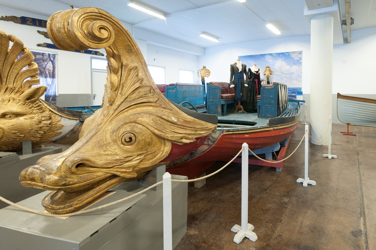 In 1783 King Gustaf III travelled to Italy. In Venice he was taken on a tour in a gold-ornamented gallery. The king also watched a splendid spectacle in the form of a regatta on the Canal Grande. A great number of decorated boats and gondolas assembled well before noon. At two o'clock in the afternoon boats with Venetian nobelmen came to pick up the king and his entourage to see the regatta. The boats were decorated with silk, canopies, parasols and flowers. The rowers were dressed in silk and adorned with silver. "The spectacel was vivid, full of splendor and distinctive character and quite dazzling", as Gundmund Jöran Adlerbeth writes in his diary from the journet. King Gustav III was very much impressed.

I order to supreise the king, master ship builder Fredrik Henrik af Chapman had "two pleasure vessels for Haga" built. Haga was a rural ground, north of Stockholm, where Gustav III at the time was creating a royal rank park. The "gondolas" were probably built in 1785 or 1786, and the heads of the boats were in all certainty made by the sculptor Hohan Törnström.

The king was "infinitley pleased", and the sloops came to be used frequently on the Brunnsviken and off Drottningholm. For rowing, boatsmen commandeered from the navy were used. The boar have been called sloops, pleasure vessels or gondolas depending on where they mentioned. The shields were originally 24 in number, with motifs from antiquity and from the twelve labors of Heracles.

After the assassination of Gustav III the sloops were forgotten and rarley used until they were pun into service again for a while during the reign of Karl XV (1859-1872). Since then, they have been stored at various places, e g near the copper tents at Haga, on Skeppsholmen and, since 1966, in the collections of the National Maritime Museum.    