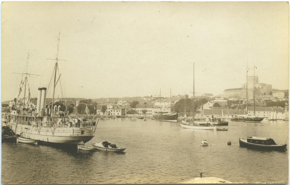 Vykort av Marstrand, med fästningen i bakgrundet till h och flera fartyg i hamnen. Till v depåfartyget, f d kanonbåten BLENDA.