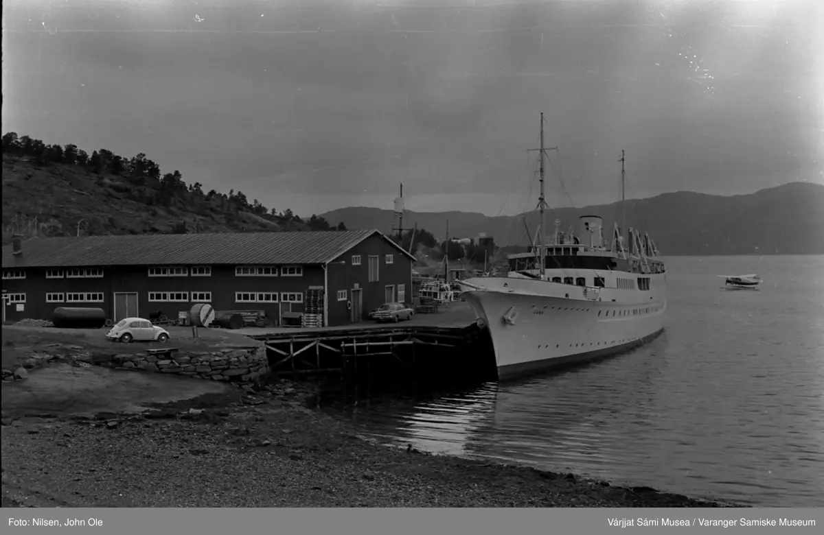 En båt ved navn "Gann" ligger ved kai i Bukta i Alta, et lite sjøfly i bakgrunnen. Alta, Juli 1967