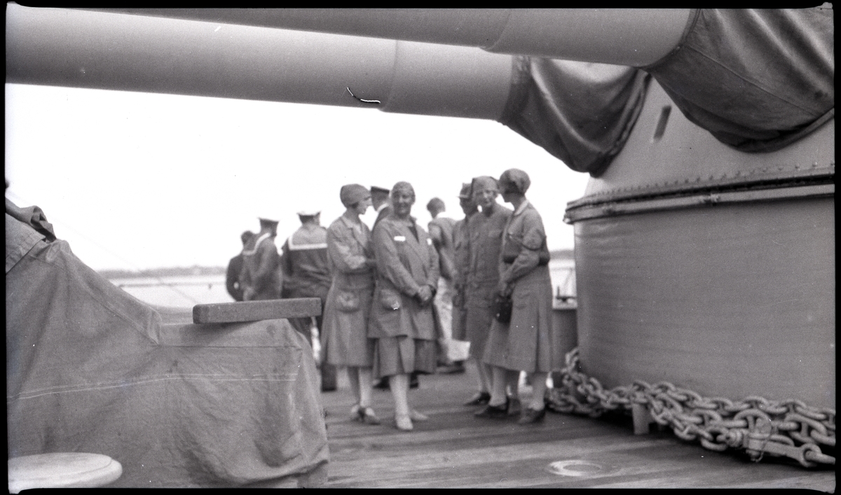 Kvinnor och flottister på däck under kanonerna, på ett pansarskepp. Andra bilder i Gunvald Bergers samling tyder på att denna bild tagits under flottuppvisningen i Göteborg 1929, men denna förmodan har inte kunnat bekräftas.