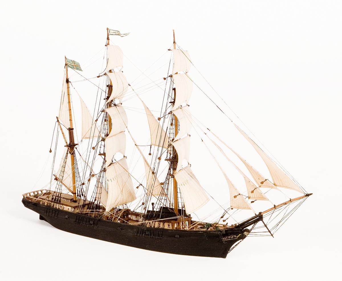 Fartygsmodell, vattenlinjemodell, hel, i block av trä, tremastade barkskeppet Hudiksvall av Hudiksvall (1864). Svartmålat skrov med galjonsbild föreställande kvinnohuvud, riggad med stående och löpande rigg, segel av papper. Två vita däckshus, två svarta livbåtar, namnvimpel på stortoppen, svensk flagga på mesantoppen.