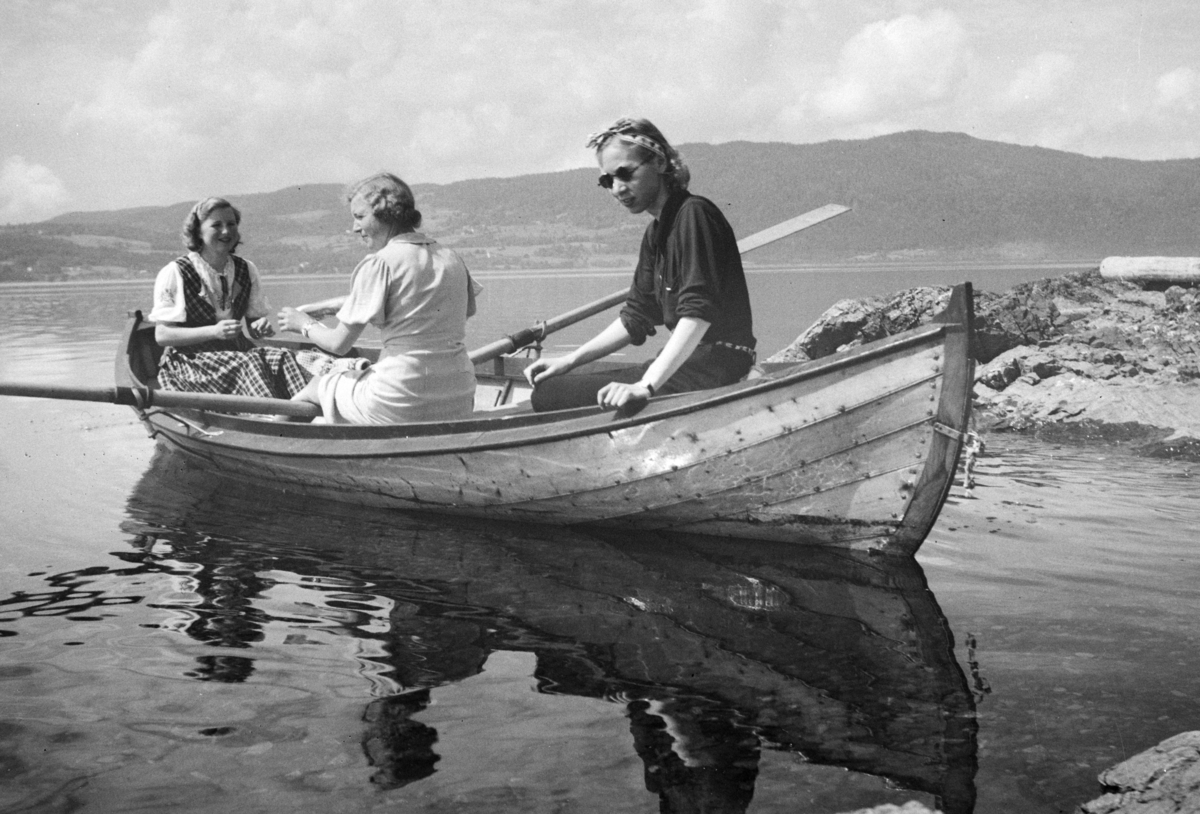 Furnes, Jessnes, Grøtodden, Robåt (dreggebåt, mjøsbåt, Hollandbåt), Til høyre sitter Lumi Johannessen, damen i midten er Ruth Oline Engebretsen, født Carlsen, født i 1915. Hun var nabo til Lumi, til venstre bak i båten sitter Ruth Oline sin søster -  Hjørdis Kristine Kjendlie, født Carlsen, i 1919. Her sittende i båten utenfor "Lia, " hytta til baker Johs. Johannessen på Jessnes i Furnes. Mjøsa. Båten er ikke malt (ant. lakkert), har utliggere for årene, typiske for mange av mjøsbåtene.