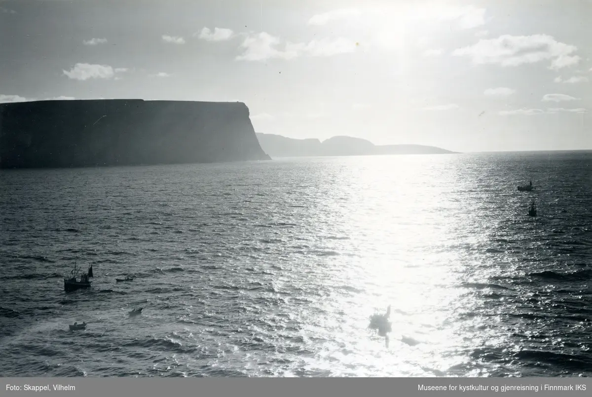 Flyfoto. Silhuett av Nordkapp-klippen. Knivskjellodden i bakgrunnen. Flere fiskebåter på sjøen. 22.08.1953.