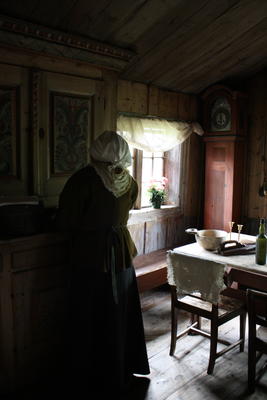 Stor-Ingri i Målstugua. Her står hun i stuerommet foran framskapet med ryggen til kamera.