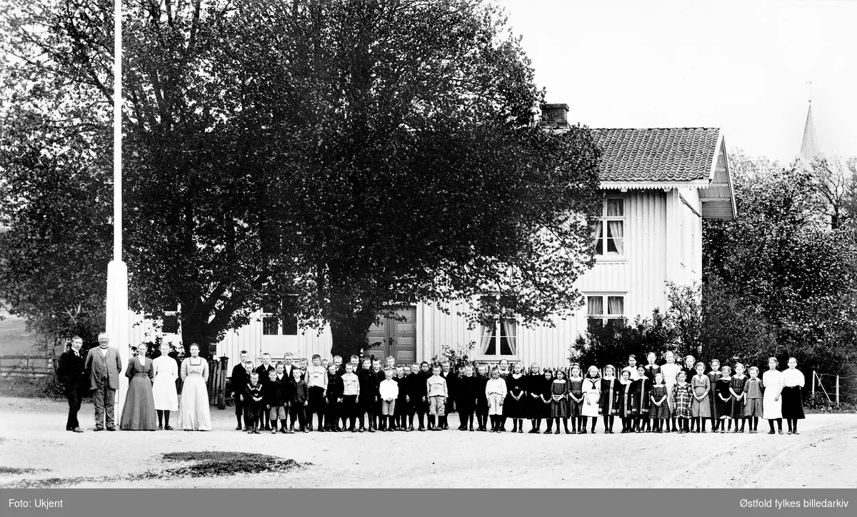 Sanne og Solli bruksskole. 
Bildet tatt utenfor skolebygningen med lærerstaben til venstre og høyre på bildet, ved flaggstangen. Guttene for seg, og jentene for seg på ei lange rekke. 
Personer ukjente. Postkort.
Til venstre lærer Halvor Vegheim og Netta Berge.