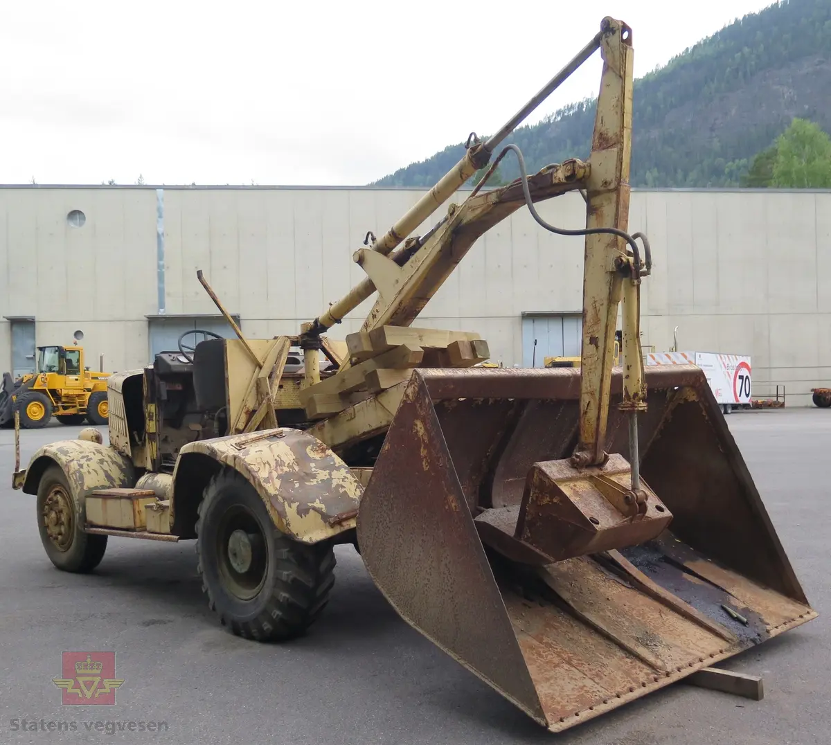Hanomag SS 100 LN. Ombygd 2 - akslet (4 hjul) maskin med både hydraulisk gravemaskin og lasteskuffe. Gul er hovedfarge (antatt grå originalt). Fra fabrikken ble typen SS 100 LN utstyrt men en vannavkjølt 6-sylindret dieseldrevet motor av typen Hanomag D85S som yter 100 Hk ved 1500 omdreininger. Motorvolum er 8,553 liter. Motornummeret skal være 60386 om motoren er den originale. Maskinens produksjonsnummer er 432528. Girkassen er av typen ZF KB60 med 4 gir framover og ett bakover, pluss overdrive. Topphastighet 65 km/t. Det elektriske anlegget er 24 V. 20 tommers hjul, opprinnelig hadde den tvillinghjul bak. Dører finnes men sitter ikke på.
Har tre merker (stempel) med ørn og hakekors samt plate fra produsenten (på torpedoveggen).
"FROSS-BUSSING" merking i fronten (antatt grill fra en Fross- Bussing).