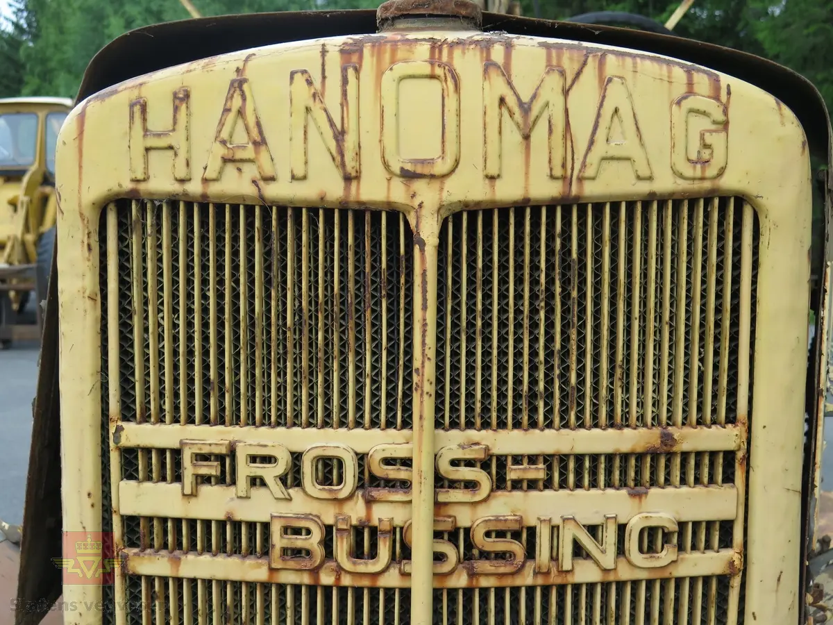 Hanomag SS 100 LN. Ombygd 2 - akslet (4 hjul) maskin med både hydraulisk gravemaskin og lasteskuffe. Gul er hovedfarge (antatt grå originalt). Fra fabrikken ble typen SS 100 LN utstyrt men en vannavkjølt 6-sylindret dieseldrevet motor av typen Hanomag D85S som yter 100 Hk ved 1500 omdreininger. Motorvolum er 8,553 liter. Motornummeret skal være 60386 om motoren er den originale. Maskinens produksjonsnummer er 432528. Girkassen er av typen ZF KB60 med 4 gir framover og ett bakover, pluss overdrive. Topphastighet 65 km/t. Det elektriske anlegget er 24 V. 20 tommers hjul, opprinnelig hadde den tvillinghjul bak. Dører finnes men sitter ikke på.
Har tre merker (stempel) med ørn og hakekors samt plate fra produsenten (på torpedoveggen).
"FROSS-BUSSING" merking i fronten (antatt grill fra en Fross- Bussing).