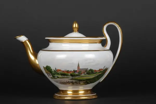 Urneformet tekanne i porselen. Tekst under bunnen som forteller at de flerfargede prosepktene over den hvite glasuren forestiller København og Christiania. Forgylte detaljer.