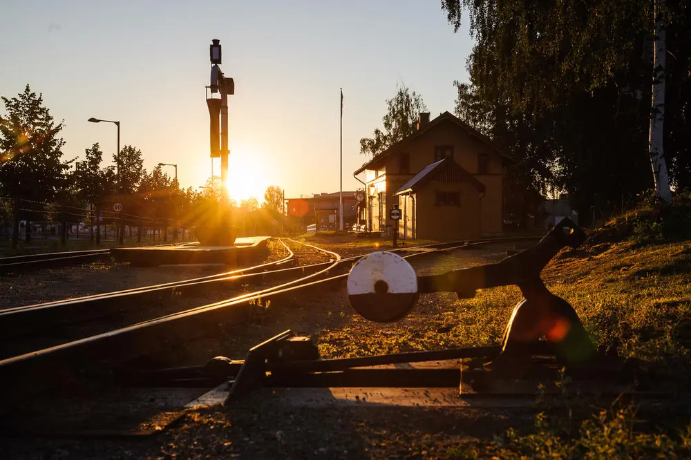 Sørumsand stasjon fotografert tidlig på morgenen. I bakgrunnen en lav morgensol og skyfri himmel. I forgrunnen en sporveksel, vanntårn og stasjonsbygningen.