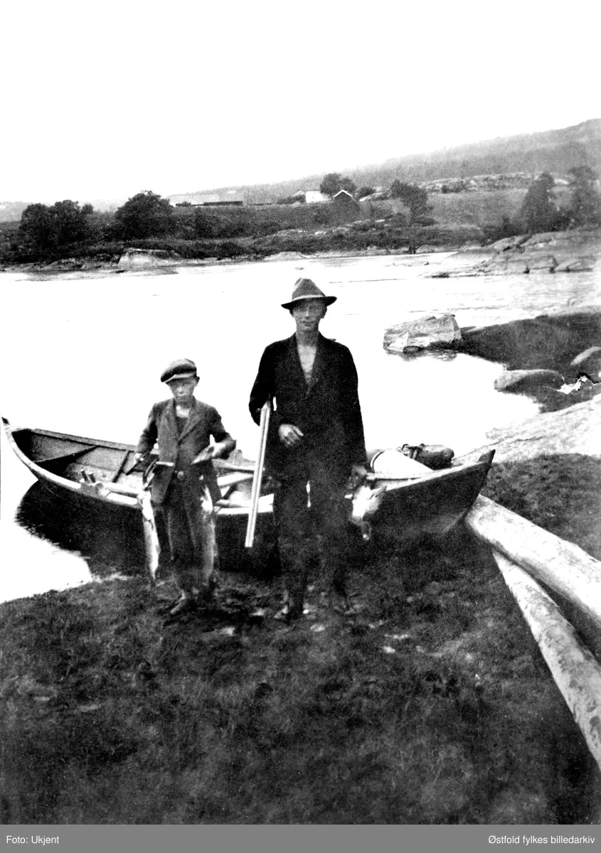 På fisketur i Glomma ved gården Lunde i Varteig ca. 1932.  Fra venstre: brødrene Johan og Arthur Lunde. Man brukte geværet til å skyte gjedde.