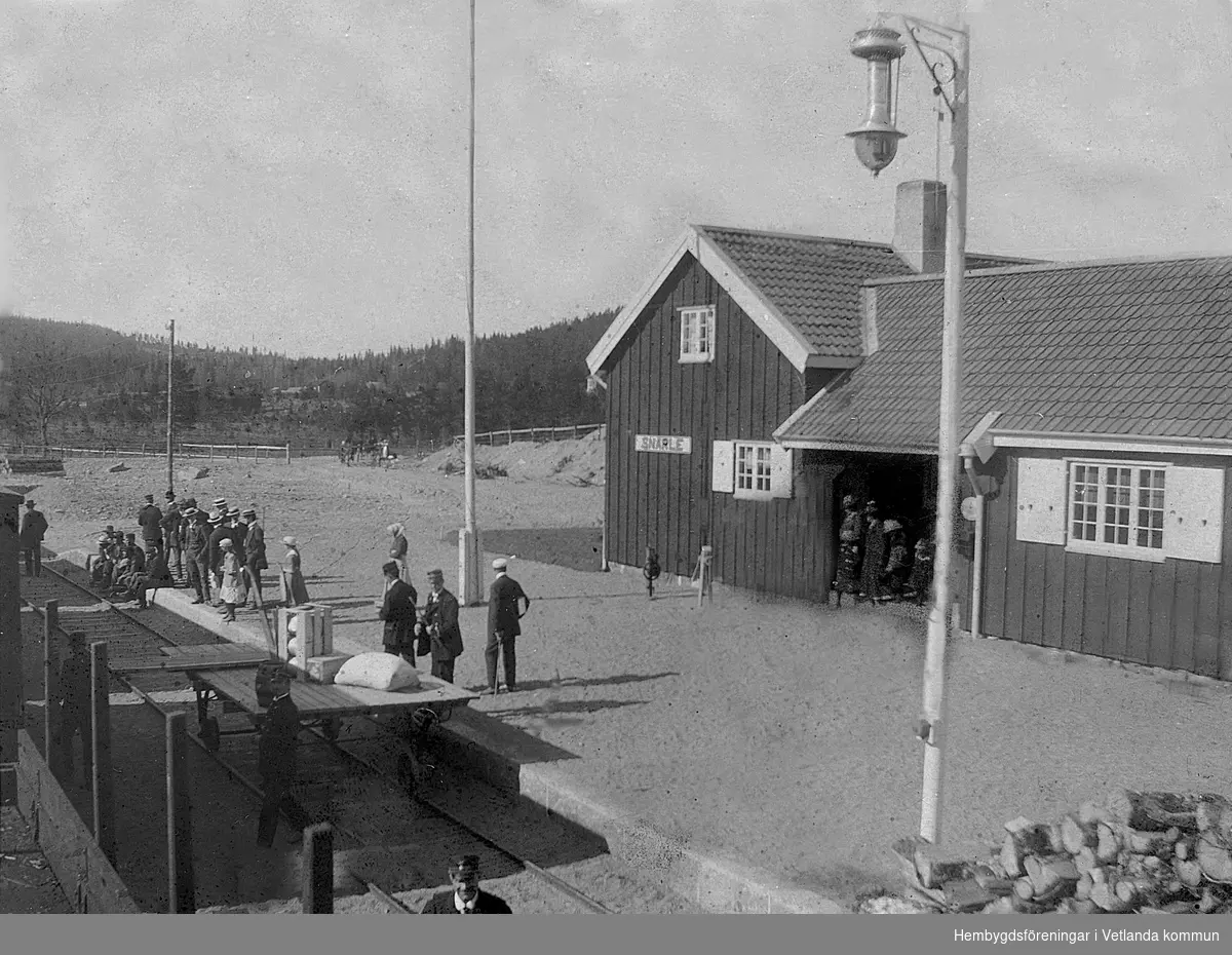 Snärle station omkring 1920. Ett godståg har kommit in och man håller på med lossning/lastning av styckegods. Till höger en dåtida platformsbelysning, där längs upp på stolpen finns en oljelampa som med en vinschanordning kunde hissas upp oc hner för att tändas eller släckas.