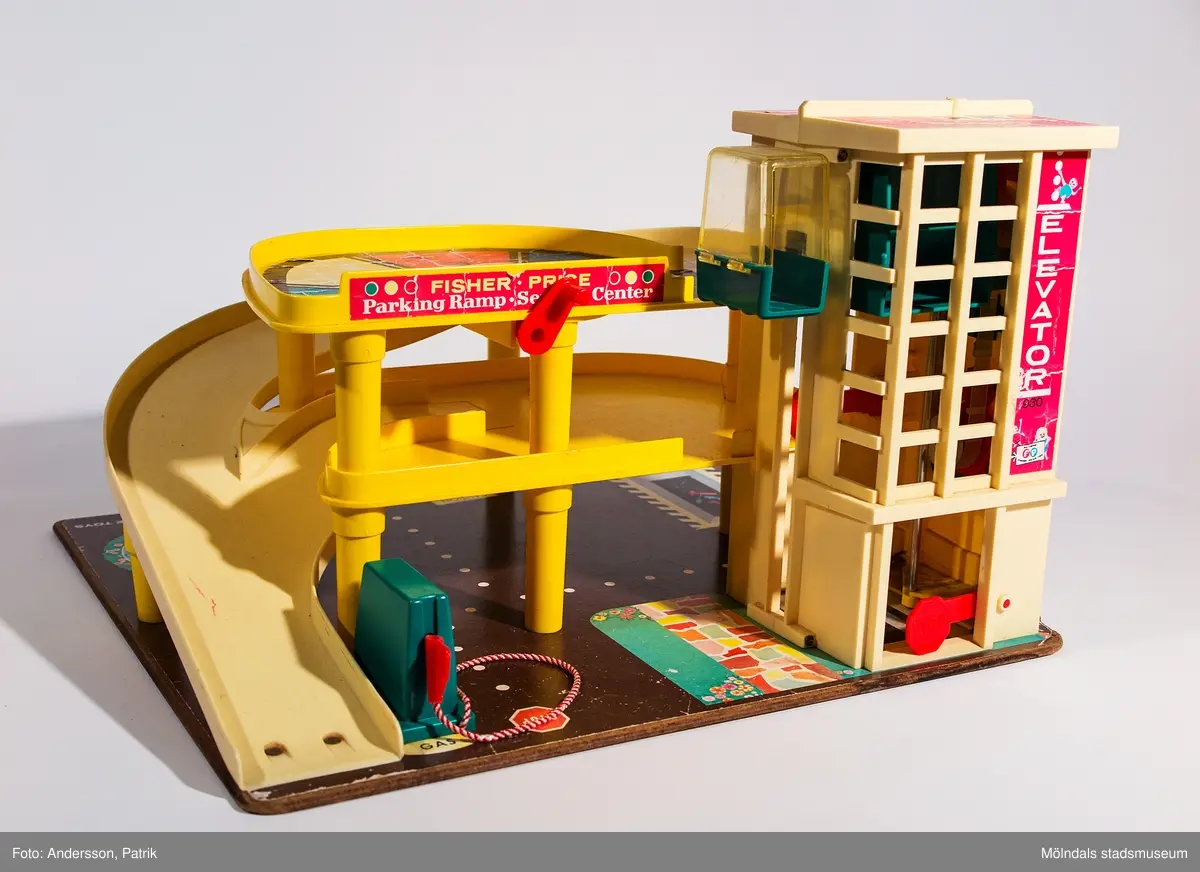 Fisher-Pricegarage från 1970-talet. Inköpt 2001 på Second Hand av givaren, vars barn har lekt med det. Garaget är i tre plan och står på en masonitplatta. Det har person-/bil-hiss med vevfunktion och pling från plan 1-3, vev att snurra vänd-platta på våning 3, tankstation på plan 1 samt två nedförsbackar från plan 2 och 3 till plan 1. Nivåskillnaderna är uppbyggda med plaststolpar vilket gör att bilar lätt åker nedför backarna.
