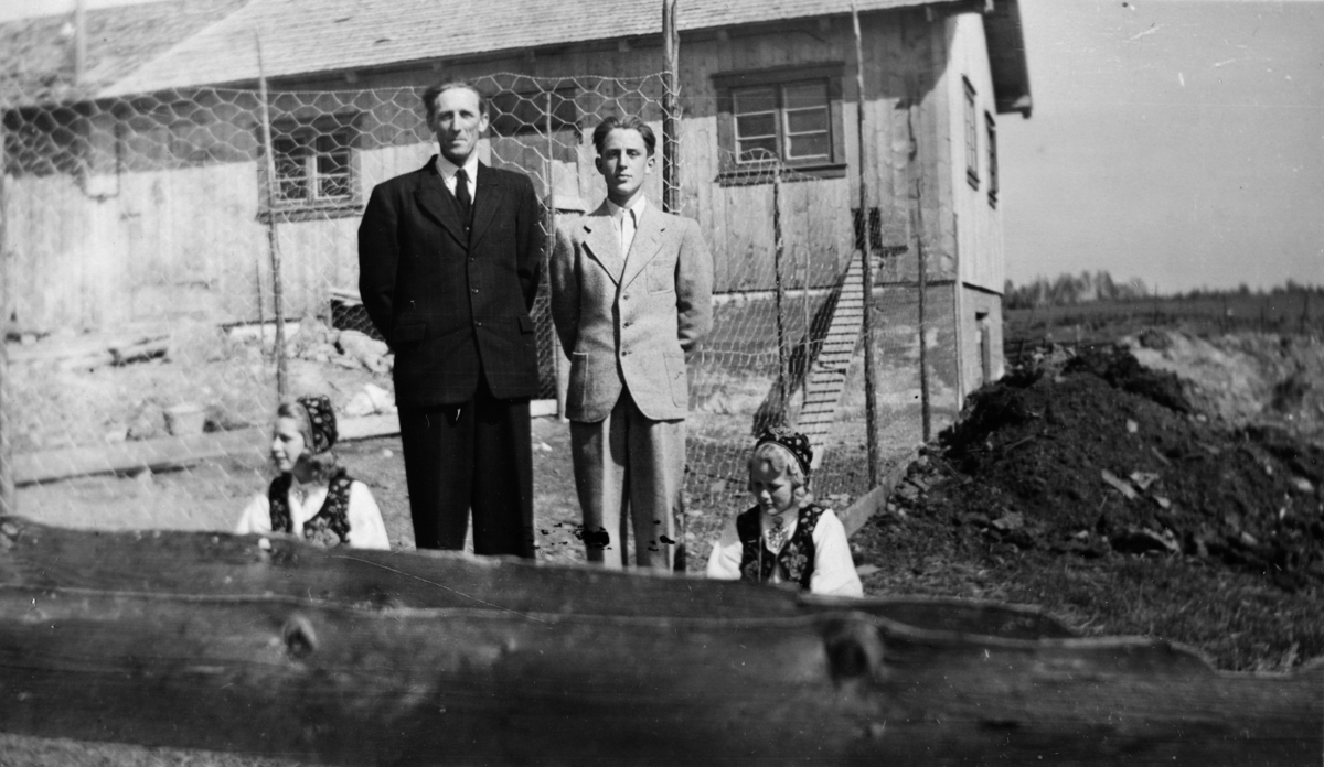 Vesterengen (85/3) 1947. Bildet er tatt i Jenny Granlis konfirmasjon. Både Jenny og søstera Aslaug fikk bunad til denne dagen. I midten: faren Martin Granli, og Aslaugs tvillingbror Leif. Fjøset i bakgrunnen er nytt og rommet tre melkekyr, gris og høner. Vi ser hønetrappa som går inn i fjøset og kvea foran.