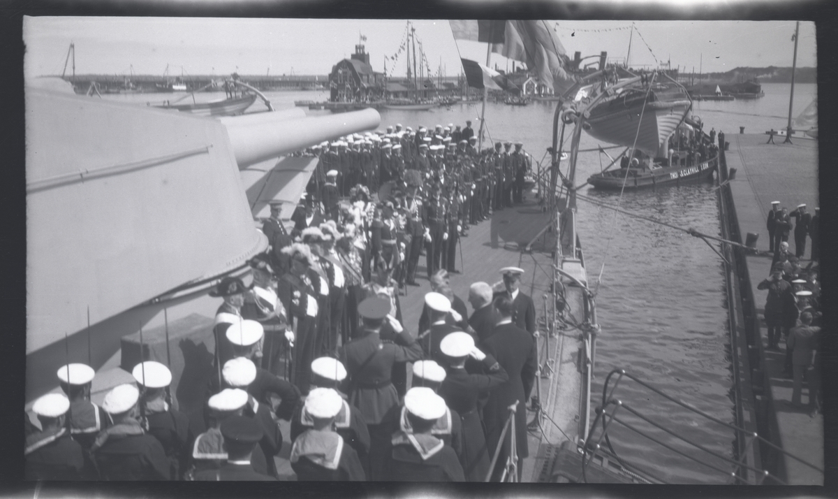 Från Gustaf V:s statsbesök i Tallinn 27-28 juni 1929. Kungen anländer på pansarskeppet SVERIGE och hälsas på däck av estniska representanter. I bakgrunden bogserbåten TUTTI från estniska handelshuset Thomas Clayhill & Son.