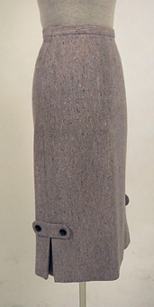 Ofodrad kjol av ull, s.k. homespun. Varpen är rosa och inslaget består av olika blå nyanser ullgarn. 
Blixtlås i vänster sida. Sprund nedtill i sidsömmarna.