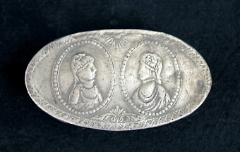 Oval snusdosa. På locket två medaljonger med kvinnobyster, sidorna och botten ornerade med omväxlande stolpar och rankor.