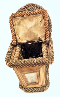 KORG, REKTANGULÄR, HANDTAG, TVÅ LOCK. ÅTTA ST INGLASADE BILDER PÅ LOCKEN OCH SIDORNA. GLAS UNDER BOTTEN. RUNT MOTIVEN FINNS STRÅN SOM I SIN TUR ÄR OMGIVNA AV RINGLANDE BUNDNA STRÅN.