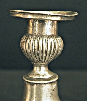 Ljusstake av tenn. Kvadratisk fotplatta med kulor i hörnen. Skaftet balusterformat. Ljushållare med godronnering.