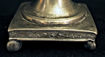 Ljusstake av tenn. Kvadratisk fotplatta med kulor i hörnen. Skaftet balusterformat. Ljushållare med godronnering.