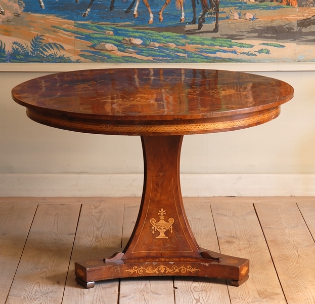 Runt bord av mahogny med intarsia. Den runda skivan vilar på ett underrede vilar på en platta i en insvängd trekantig form. I vardera ända av plattan en fot i form av en rektangel. Intarsia på underredet, foten samt bordsskivan.