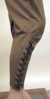 Konfektionssydd ridbyxa av kraftigt bomullstyg vävt i tuskaft. Modellen är sydd med sprund i sidorna vilka knäpps med knappar, två snedställda fickor framtill, linning som knäpps i sidorna  med metallspännen samt sprund nedtill på byxbenen. Dessa sprund hålls samman med en snörning. byxbenen är skurna med mycket vidd upptill och är åtsittande nedtill. Anm. enligt accessionskatalog: "Inköpta 1925 - 1930."