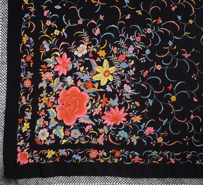 Schal, av svart crepetyg med broderier över hela ytan, i de fyra hörnen större blommönster i flera färger. Lång frans. Möjligen tillverkad i Kina, handgjord. Märkt "85583 FL".