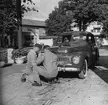 Två män utför någon form av reparation/justering på ena strålkastaren på en Volvo PV 444KS av 1956 års modell.