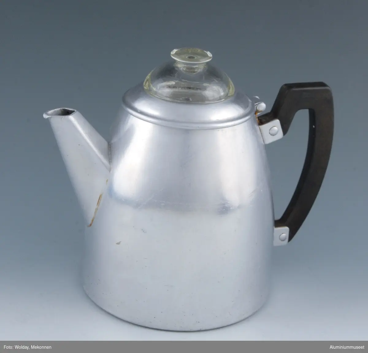 Teknikk: En tykk rondell er presset og tynnet i veggen til et sylindrisk hulkar. Hulkarret er renskåret og konpresset i en hydraulisk presse til ferdig utvendig form. Kjelen er lokket og stanset for feste av håndtak med lokk, og det er lokket hull for tut. Tuten er laget av platemateriale, den er knekket og sveiset. Tuten er loddet til kjelen. Kjelen er polert. Lokket er håndtrykket, det er lokket hull for glasslokk og et hengsel-øre er påloddet.Bøylen er påklinket etter eloksering. Kannen leveres med innsats for trakting av kaffe.
Form: Konisk form
