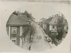 Östra Sjögatan på 1870-talet, sedd från Kavaljeren. I förgrunden till vänster Kv Borgmästaren (Östra Sjögatan 1) i dess ursprungliga skick: Väggar panelade och röda med vita knutar, taklist med träsnitt. Framför huset i gatkanten en lind. I fonden skymtar Kantorsporten, en av de nu rivna portarna i Kalmars stadsmur. Framför porten syns eventuellt en av stadens brunnar.