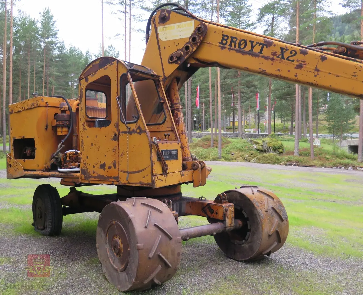 Gravemaskin, hjulgående. 2 jernhjul foran og 2 gummihjul bak. Maskinen er oransje med svart sete. Motoren er en 4-sylindret dieseldrevet type fra Perkins. Gravemaskinen var ikke selvgående, men forflyttet seg med gravearmen under arbeid. Ved transport mellom arbeidsstedene hektet en skuffen i lasteplanet og løftet opp "forhjulene" slik at den ble transportert som en henger.