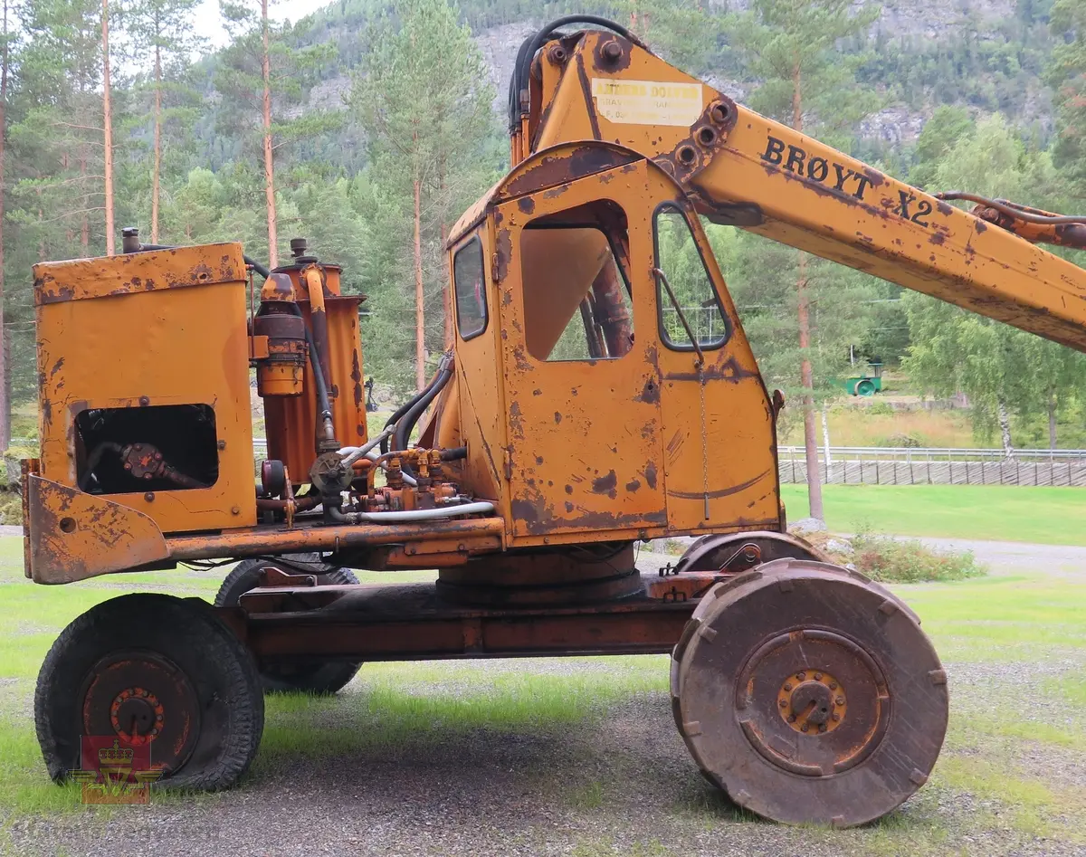Gravemaskin, hjulgående. 2 jernhjul foran og 2 gummihjul bak. Maskinen er oransje med svart sete. Motoren er en 4-sylindret dieseldrevet type fra Perkins. Gravemaskinen var ikke selvgående, men forflyttet seg med gravearmen under arbeid. Ved transport mellom arbeidsstedene hektet en skuffen i lasteplanet og løftet opp "forhjulene" slik at den ble transportert som en henger.