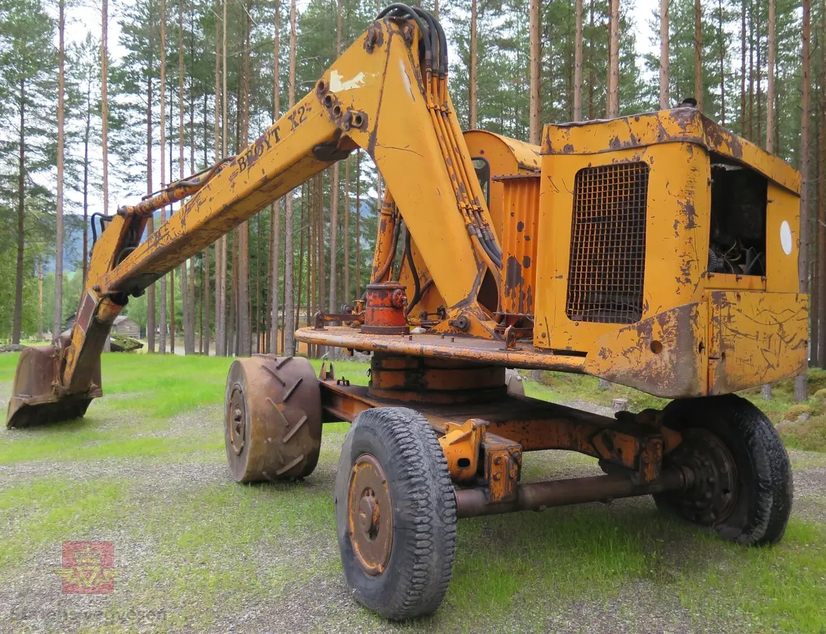 Gravemaskin, hjulgående. 2 jernhjul foran og 2 gummihjul bak. Maskinen er oransje med svart sete. Motoren er en 4-sylindret dieseldrevet type fra Perkins. Gravemaskinen var ikke selvgående, men forflyttet seg med gravearmen under arbeid. Ved transport mellom arbeidsstedene hektet en skuffen i lasteplanet og løftet opp "forhjulene" slik at den ble transportert som en henger.