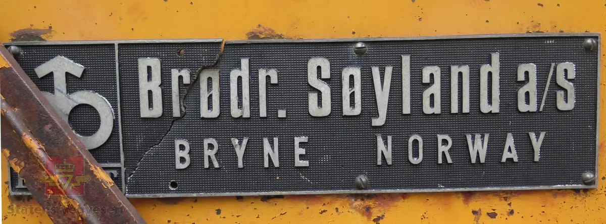 Gravemaskin, hjulgående. 2 jernhjul foran og 2 gummihjul bak. Maskinen er oransje med svart sete. Motoren er en 4-sylindret dieseldrevet type fra Perkins. Gravemaskinen var ikke selvgående, men forflyttet seg med gravearmen under arbeid. Ved transport mellom arbeidsstedene hektet en skuffen i lasteplanet og løftet opp "forhjulene" slik at den ble transportert som en henger.