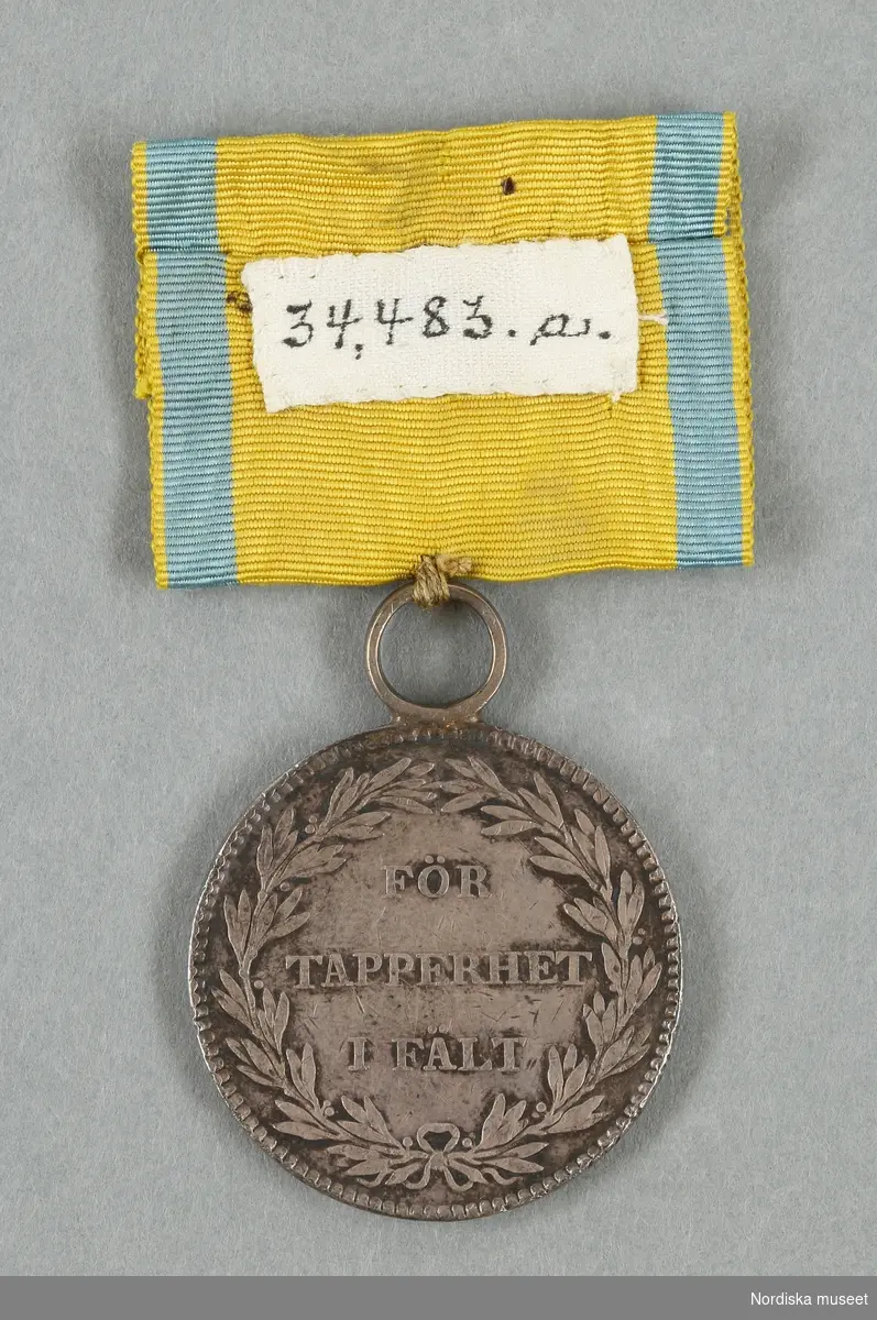 Huvudliggaren:
"Medalj och ordenstecken. Se 34.443 [= 34.443-34.485 samlade af friherre Bennet.] 
a) Medalj  i silfver. för tapperhet i fält. Åtsidan: Kungl. Svärdsordens riddarstjärna. Jmfr. Hildebrand B E, Sveriges och svenska konungahusets minnespenningar, praktmynt och belöningsmedaljer del 2, sid 291, nr 25. I gult band af sidenrips med ljusblå ränder i kanterna. 
b) Ordenstecken. .
Ink. ss. 34.424 [=ink. ss. 34.422  jämte 34.425-34.485]. [34.422=Ink. af byggmästare E. A. Boman i Stockholm 8/1 1883]"