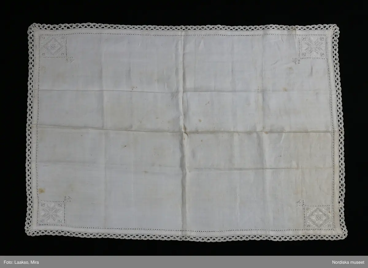 Fyrkantigt kläde av handvävd vit linnelärft. 1 cm bred fåll sydd med r enkel utdragssöm,   i varje hörn ett kvadratiskt broderi 8 x 8 cm med i rätlinjig plattsöm och utskuren söm, olika mönster i varje hörn. Klädet kantat med 2,5 cm bred knypplad uddspets av ålderdomlig flätslagstyp. 
Denna typ av linnekläde från Värendsområdet hör till samma dräktområde som Skåne och Blekinge där liknande kläden använts till högtidsdräkten som handkläde och vid kyrkbesök som bokkläde kring psalmbokem. Vid stora kalas har det även kunnat användas som förningsduk kring medförda varor.  Vid begravningar har det även kunnat bäras som huvudduk.
/Berit Eldvik 2010-06-23
Armklädet har kommit från Djuramåla Jostagård i Tingsås sn. dit kom Johanna Maria Nilsdotter genom giftermål. Hon var dotter till Elna Håkansdotter Nilsson 
( 1791-1879) se 63.093/ uppgift från Birgitta Blixt 2012. /Berit Eldvik
