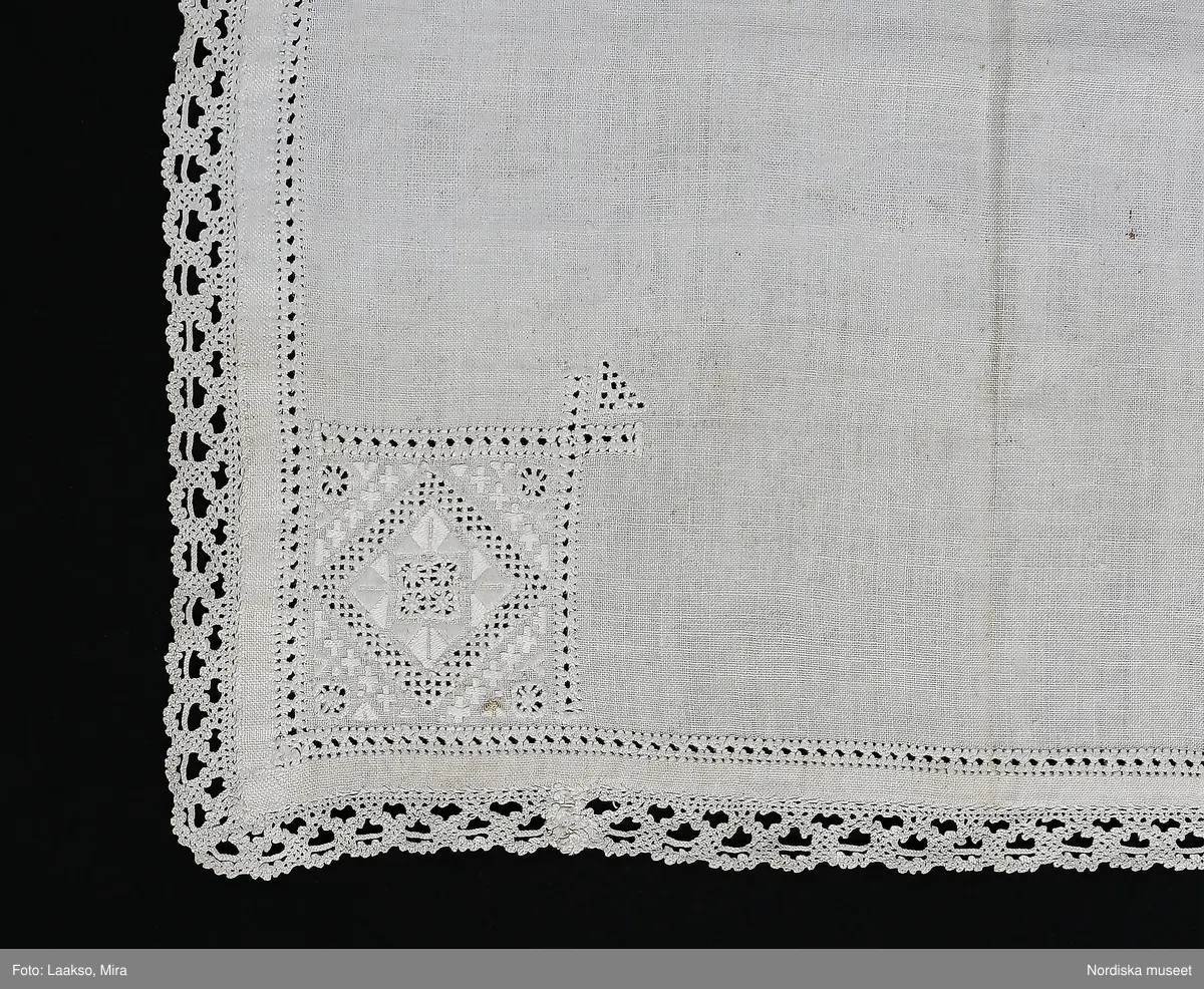 Fyrkantigt kläde av handvävd vit linnelärft. 1 cm bred fåll sydd med r enkel utdragssöm,   i varje hörn ett kvadratiskt broderi 8 x 8 cm med i rätlinjig plattsöm och utskuren söm, olika mönster i varje hörn. Klädet kantat med 2,5 cm bred knypplad uddspets av ålderdomlig flätslagstyp. 
Denna typ av linnekläde från Värendsområdet hör till samma dräktområde som Skåne och Blekinge där liknande kläden använts till högtidsdräkten som handkläde och vid kyrkbesök som bokkläde kring psalmbokem. Vid stora kalas har det även kunnat användas som förningsduk kring medförda varor.  Vid begravningar har det även kunnat bäras som huvudduk.
/Berit Eldvik 2010-06-23
Armklädet har kommit från Djuramåla Jostagård i Tingsås sn. dit kom Johanna Maria Nilsdotter genom giftermål. Hon var dotter till Elna Håkansdotter Nilsson 
( 1791-1879) se 63.093/ uppgift från Birgitta Blixt 2012. /Berit Eldvik