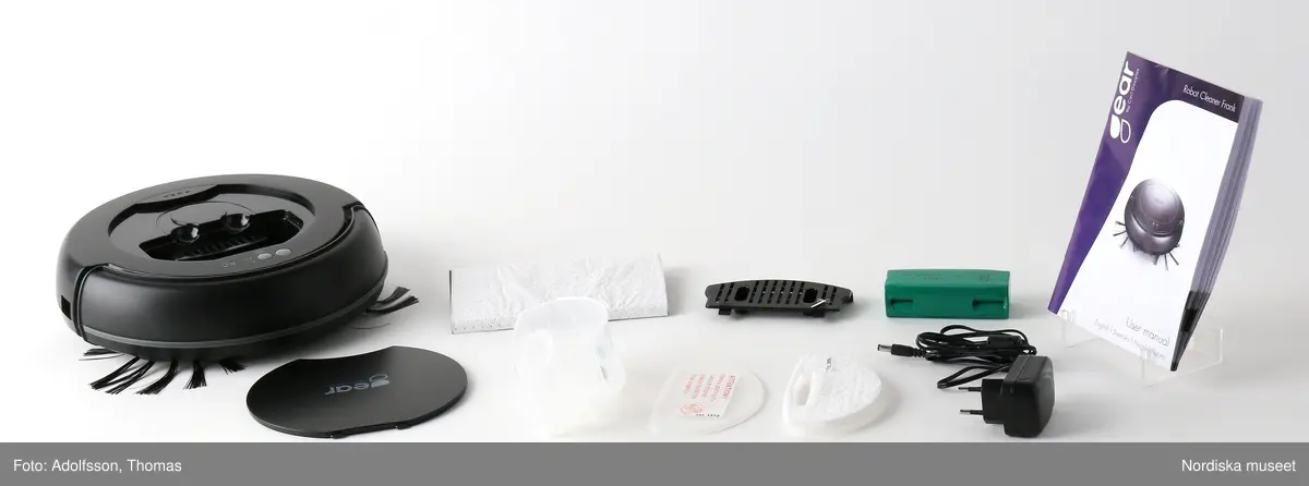 Automatisk hushållsdammsugare, så kallad minirobotdammsugare, Robot Vacuum Cleaner Frank av märket Gear by Carl Douglas. Dammsugaren en låg cylinder av svart plast. Stötdämpare längs en del av kanten. På ovansidan kontrollpanel med strömbrytare samt en lucka med texten "Gear by Carl Douglas" innehållande dammbehållare och filter.

Undertill finns intagsventil för damm och smuts, två drivhjul, ett litet främre hjul och två runda sidoborstar med långa spröt av nylontrådar. Här finns också en dammpappershållare med fastsittande dammpapper för moppning, en batterilucka och trappsensorer. Batteriet förvärvas av bevarandeskäl inte utan återvinns efter fotografering. Till dammsugaren hör också en adapter med svart sladd och stickpropp samt en bruksanvisning, Robot Cleaner Frank User manual, på flera språk.
/Maria Maxén 2017-01-11