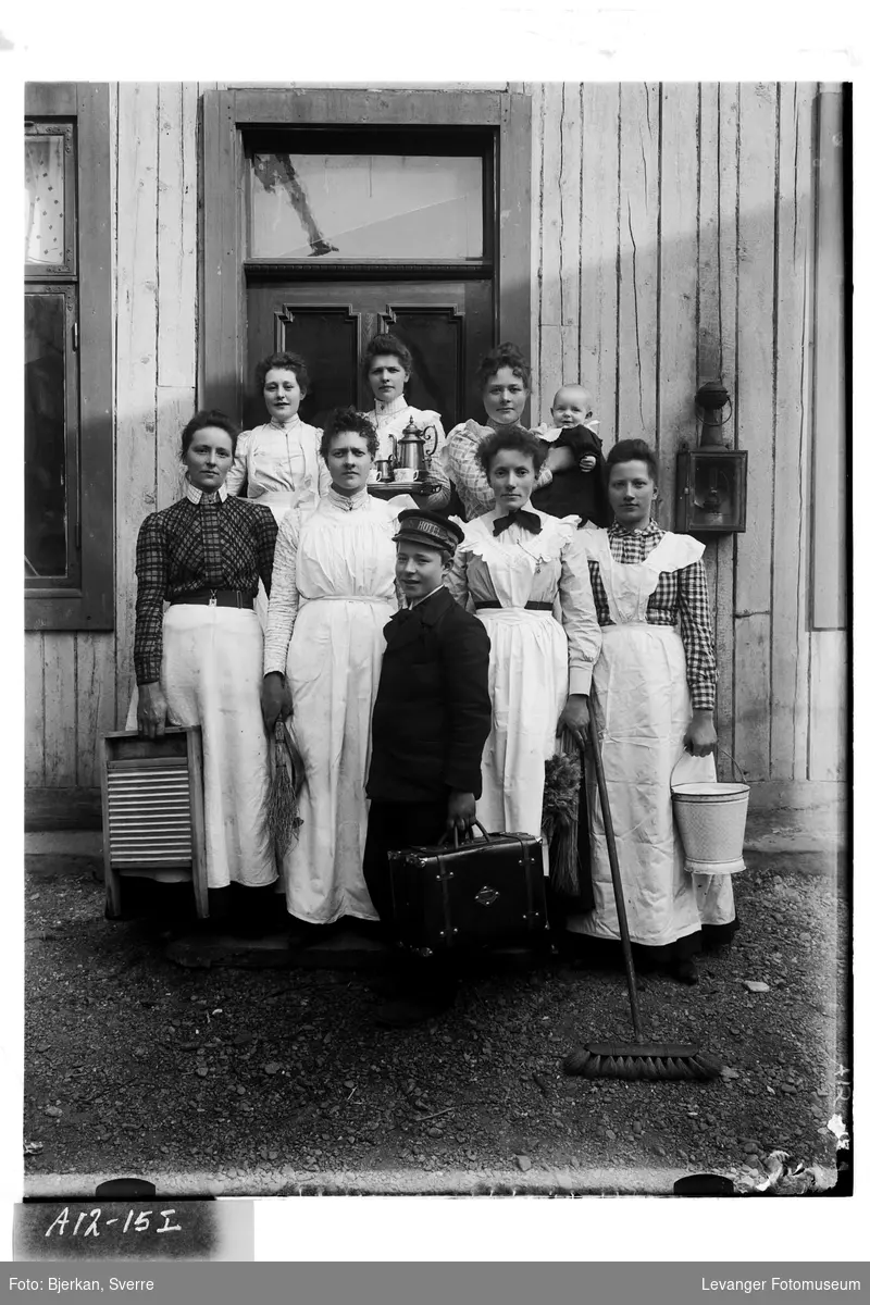 Gruppe kvinner  utstyrt med bøtter og vaskebrett, kaffeservise, og en gutt med reiseveske.