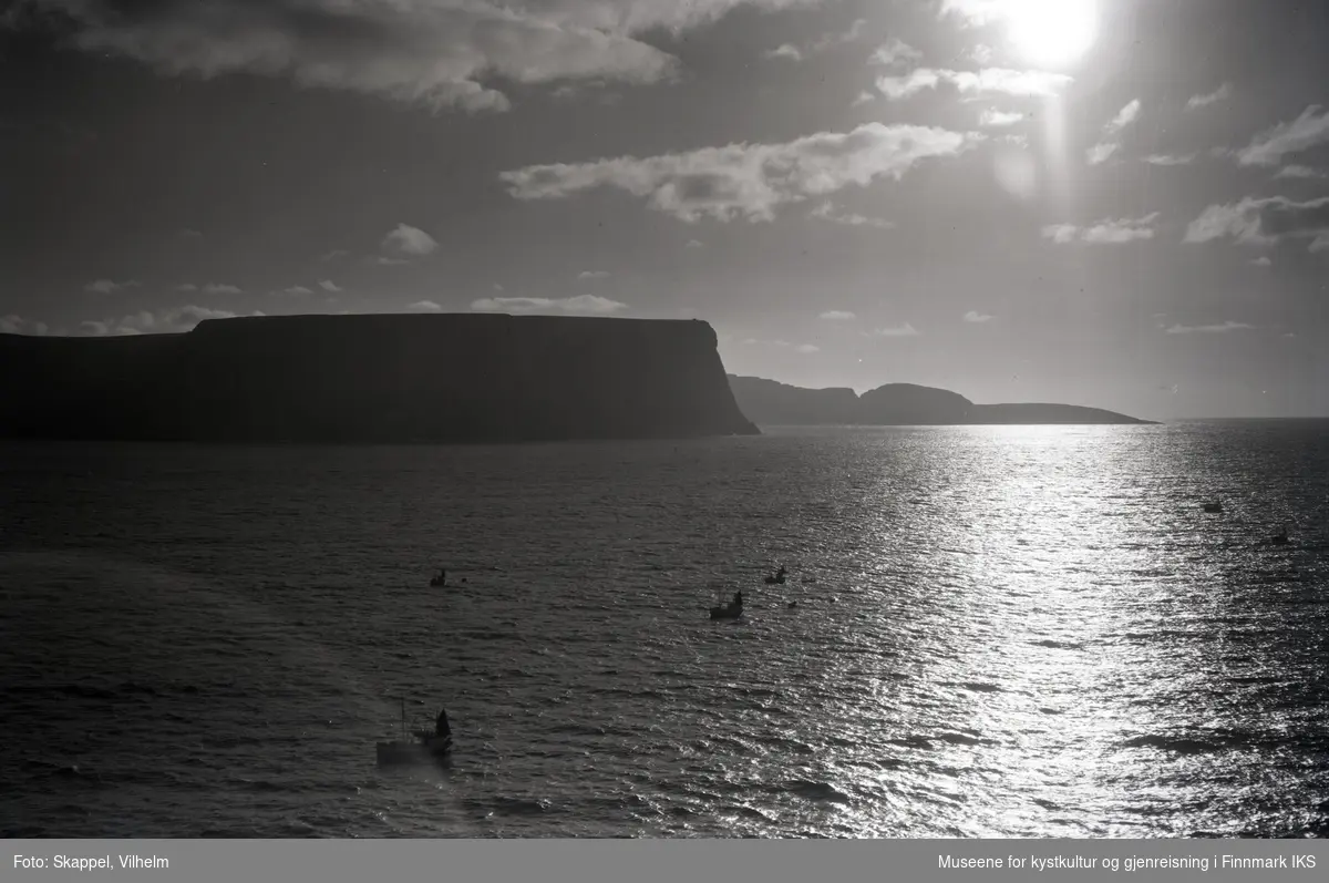 Flyfoto. Silhuett av Nordkapp-klippen. Knivskjellodden i bakgrunnen. Flere fiskebåter på sjøen. 22.08.1953.