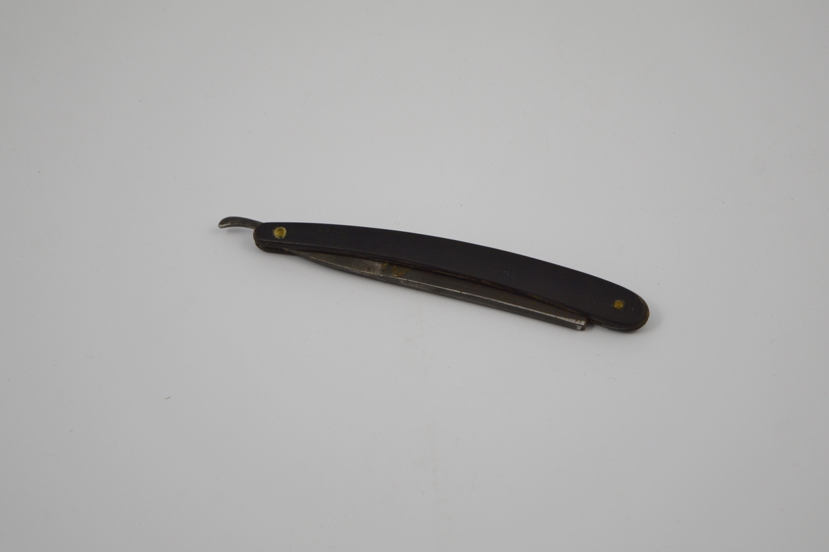 Sammenleggbar barberkniv med rett egg. Knivbladet har konisk tverrsnitt. Bladet munner ut i tynt skaft
med en krumning som holdegrep med fingeren. Skaftet er naglet fast til
kniven. Består av to deler som fungerer som beskyttelse i sammenlagt
stilling.