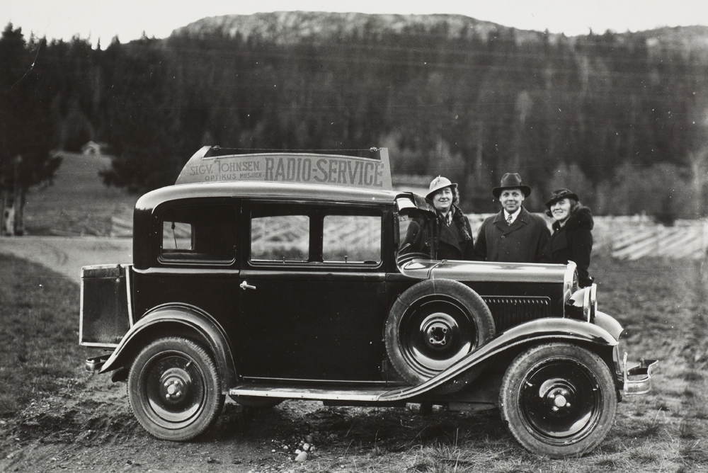 Fra venstre: Amanda og Sigvald Johnsen og Selma Andreassen (?). Ved bilen til Sigvald med reklameskilt på taket.