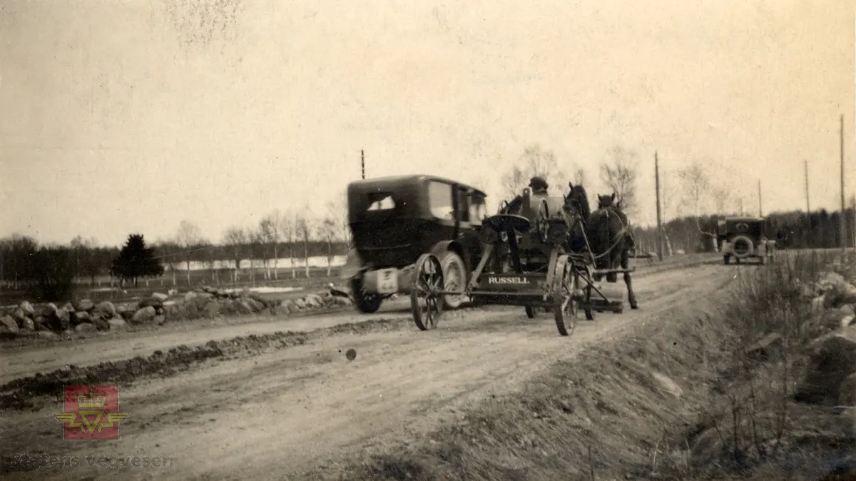 Amerikansk veghøvel "Russel Grader"  i arbeid i Østfold 1924, i følge merking.  Ref. til "Meddelelser fra Veidirektøren", Nr. 47-mai 1924. Artikkel om "Prøve med den amerikanske veihøvel "Russel Grader" samt skrapning av veibanen med "Western" skrape", av overingeniør Thor Olsen. Befaring  med vegdirektoratets og Østfold fylkets ingeniører.  Andre bilder av veghøvelen som er illustrert i artikkelen vises i bilde 2/5 og 3/5. Bilde 4/5: "Skraperne av "Western"-typen forarbeides som nævnt ved fylkets verksted og utstyres nu med en fast arm paa den ene side for styring av hele redskapen foruten den bevægelige for stillingen av bladene , som det vil sees av fig. 5". Bilde 5/5: Vedlikeholdsarbeid med amerikansk vegskrape utføres i Østfold.