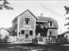 Kungsgatan 4 Karlsborg, Hellmérs livsmedel år 1924. På verandan Assar (född 1920), Anders (född 1885-1943) och Hildur (1891-1938) Hellmér. Huset byggdes 1917. Affären grundades av Anders Hellmér och Esaias Sandberg. 2 st förstoringar 30 x 40 cm. Neg finns.