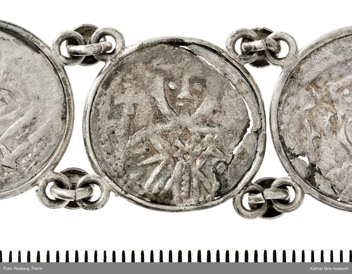 KLM 14507 Myntfynd, ett armband, bildat av silvermynt. Armbandet består av åtta infällda mynt, varav ett har lossnat från sin inramning. Mynt från Valdemar I:s tid, samt ärkebiskop Absalon, 1100-talets slut. Mynten i armbandet härstammar från ett jordfynd av ca 30 stycken likadana mynt, hittade i jorden på Åby prästgårds ägor omkr 1885. Av de nu befintliga åtta stycken, är präglade för Knut VI, Lund
