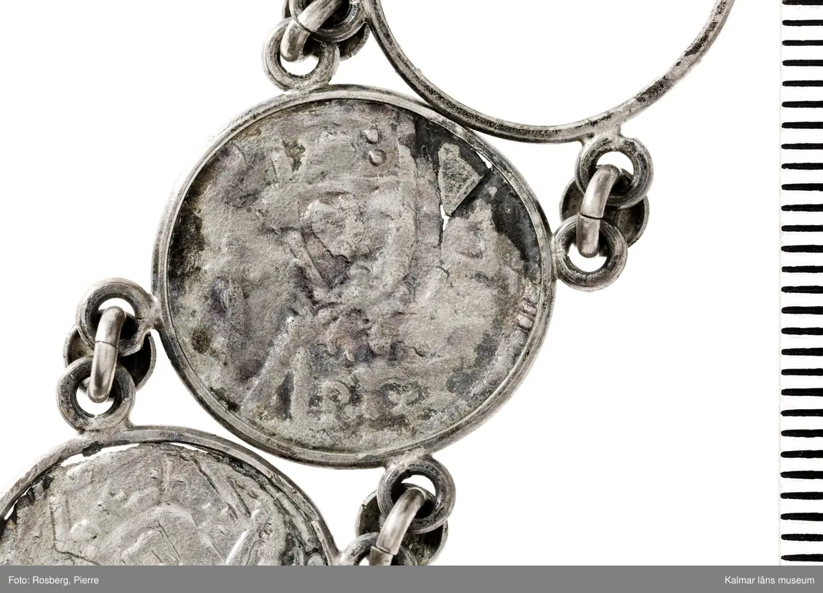 KLM 14507 Myntfynd, ett armband, bildat av silvermynt. Armbandet består av åtta infällda mynt, varav ett har lossnat från sin inramning. Mynt från Valdemar I:s tid, samt ärkebiskop Absalon, 1100-talets slut. Mynten i armbandet härstammar från ett jordfynd av ca 30 stycken likadana mynt, hittade i jorden på Åby prästgårds ägor omkr 1885. Av de nu befintliga åtta stycken, är präglade för Knut VI, Lund