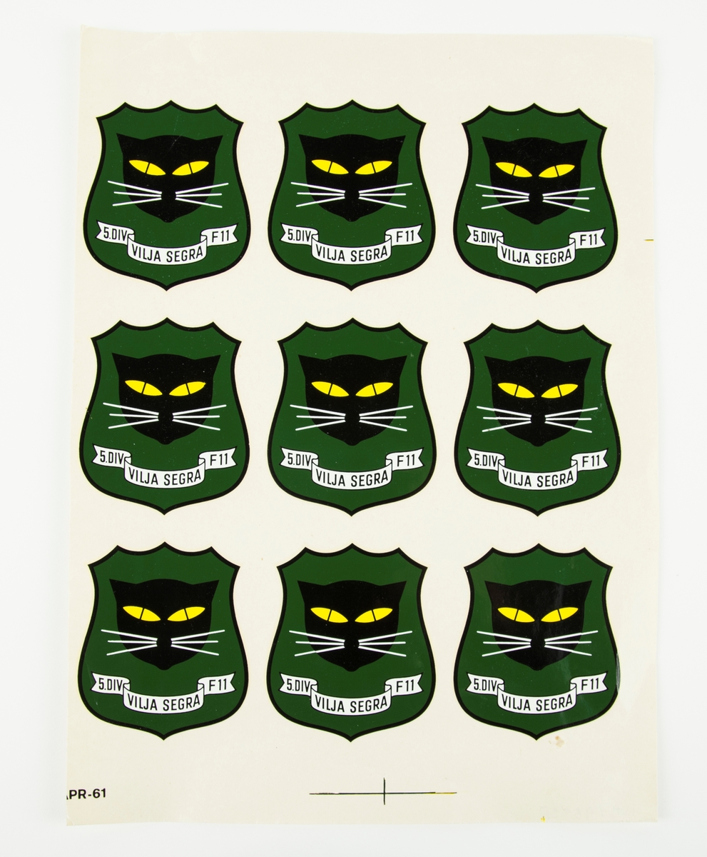 Nio hjälmdekaler på ett ark. Divisionsemblem för Södermanlands flygflottilj 5/F11 Skavsta, Nyköping.
Dekalen är utformad som en sköld med en svart katt med gula ögon på en grön bakgrund. På dekalen står: 5. Div Vilja Segra F11.